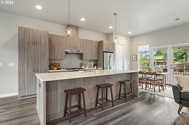 kitchen with dark hardwood / wood-style floors, stainless steel fridge, decorative light fixtures, and a center island with sink