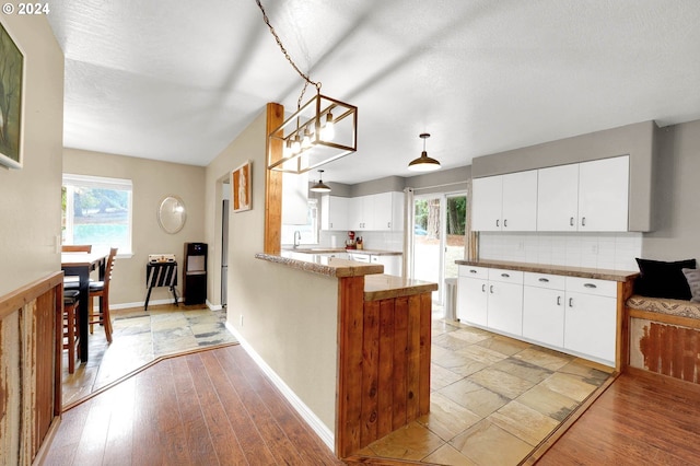 kitchen with kitchen peninsula, decorative backsplash, white cabinetry, light hardwood / wood-style flooring, and decorative light fixtures