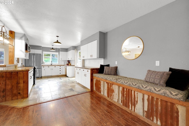 kitchen with decorative backsplash, light hardwood / wood-style flooring, stainless steel fridge, white cabinetry, and a textured ceiling