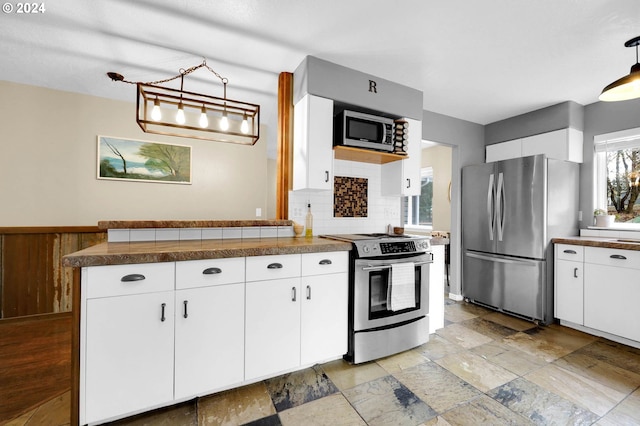 kitchen featuring white cabinetry, stainless steel appliances, tasteful backsplash, and hanging light fixtures