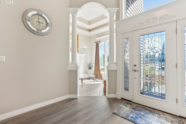 entrance foyer featuring hardwood / wood-style flooring, a raised ceiling, and ornate columns