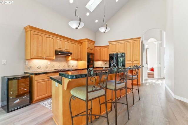 kitchen featuring black appliances, a kitchen island with sink, high vaulted ceiling, and a skylight