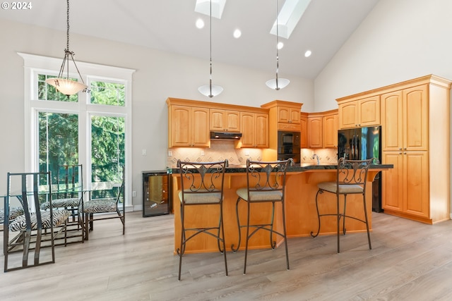 kitchen featuring a skylight, high vaulted ceiling, backsplash, a kitchen bar, and a kitchen island with sink