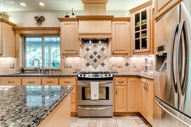 kitchen featuring tasteful backsplash, light brown cabinets, stainless steel appliances, and dark stone countertops