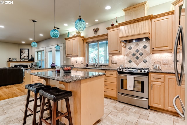 kitchen featuring light brown cabinets, stainless steel appliances, a sink, a center island, and dark stone countertops