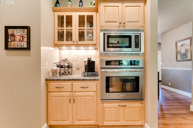 kitchen featuring light brown cabinets, light wood-style floors, appliances with stainless steel finishes, decorative backsplash, and glass insert cabinets