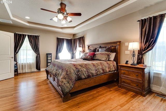 bedroom featuring a ceiling fan, a raised ceiling, visible vents, and light wood-style floors