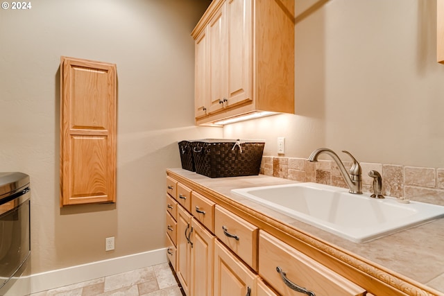 kitchen featuring light countertops, stone finish floor, light brown cabinets, a sink, and baseboards