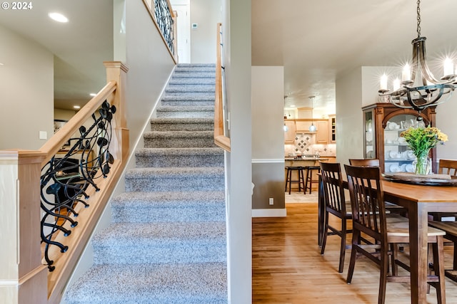 staircase with recessed lighting, wood finished floors, and a notable chandelier