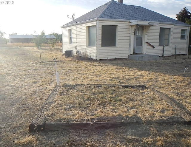 view of front of property featuring a shingled roof, a chimney, and central AC unit