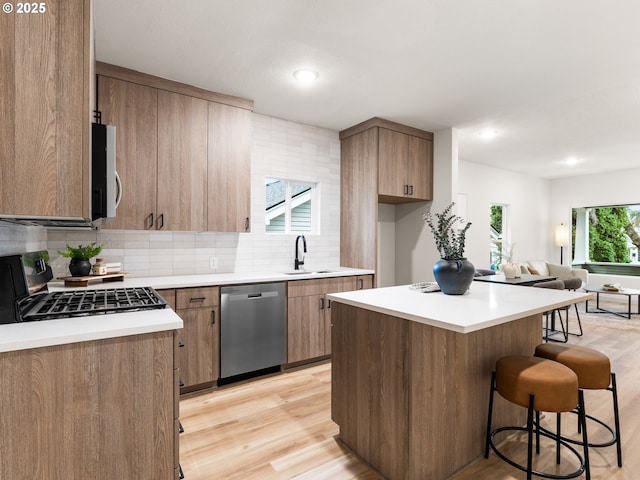 kitchen featuring appliances with stainless steel finishes, a breakfast bar area, light wood-style floors, and a sink