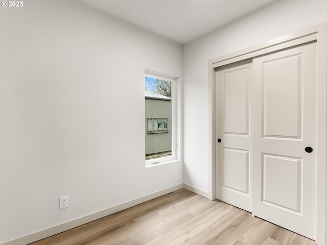 unfurnished bedroom featuring a closet, light wood-type flooring, and baseboards