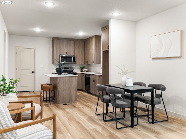 kitchen featuring light wood finished floors, a kitchen bar, light countertops, decorative backsplash, and stainless steel appliances