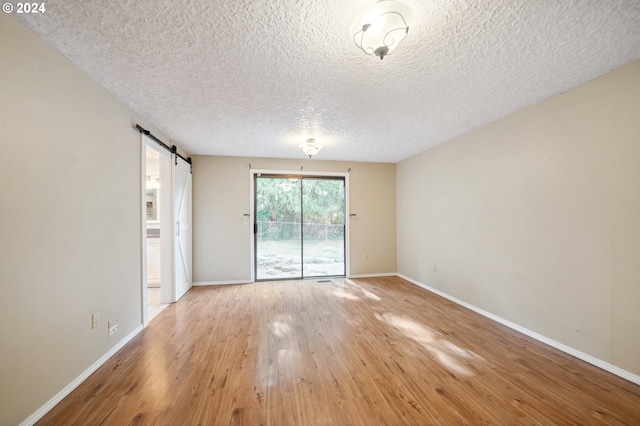 empty room featuring a barn door, light wood-type flooring, and a textured ceiling