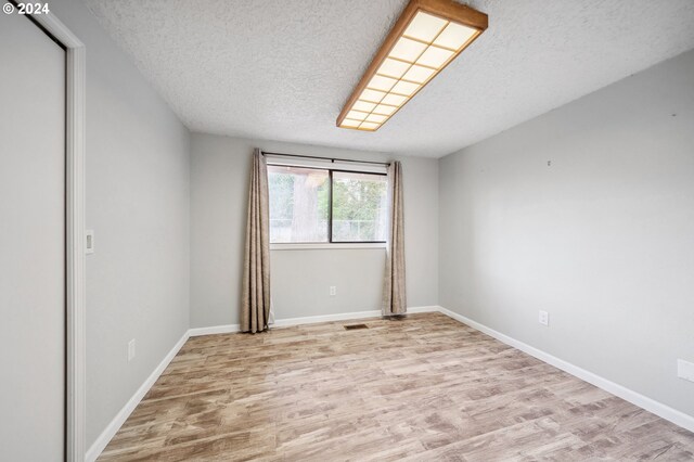 spare room with a textured ceiling and light hardwood / wood-style floors