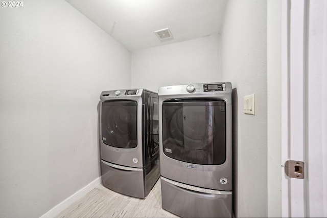 clothes washing area with washer and clothes dryer and light hardwood / wood-style floors