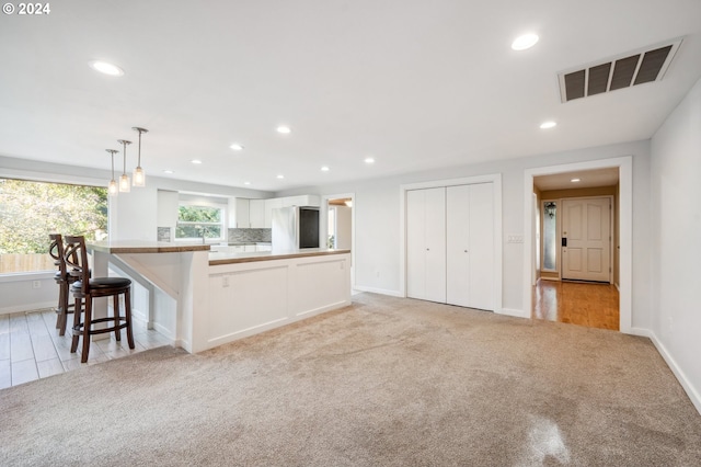 kitchen featuring stainless steel refrigerator, white cabinetry, hanging light fixtures, a breakfast bar area, and light colored carpet