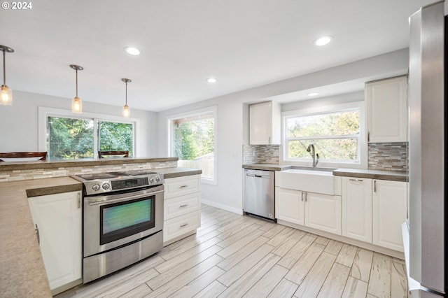 kitchen with decorative light fixtures, appliances with stainless steel finishes, sink, decorative backsplash, and white cabinetry