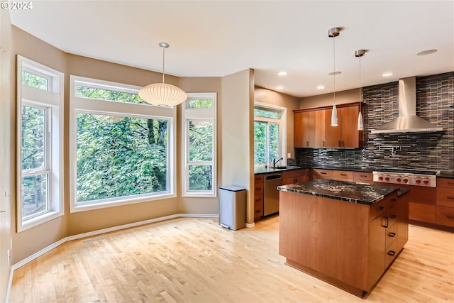 kitchen with appliances with stainless steel finishes, wall chimney range hood, backsplash, light hardwood / wood-style floors, and a kitchen island