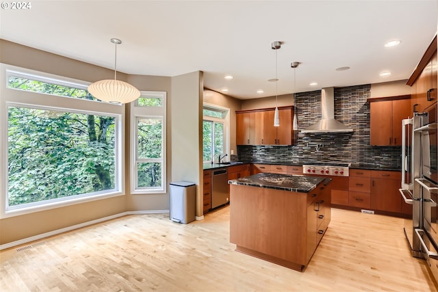 kitchen featuring light hardwood / wood-style flooring, a center island, stainless steel appliances, wall chimney exhaust hood, and decorative backsplash