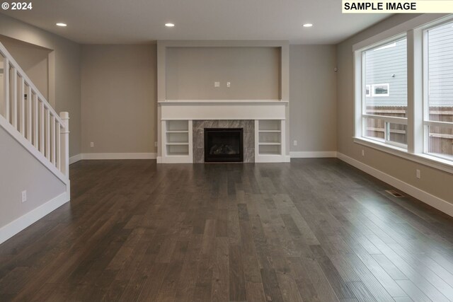 unfurnished living room with dark hardwood / wood-style flooring, a tile fireplace, and built in shelves