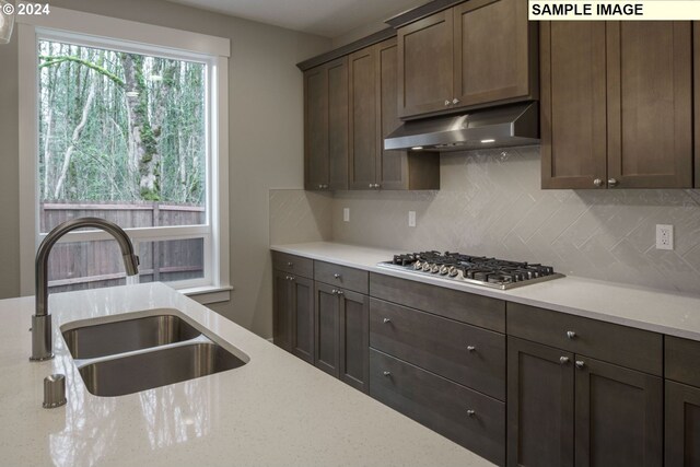 kitchen with light stone countertops, backsplash, stainless steel gas stovetop, sink, and dark brown cabinets