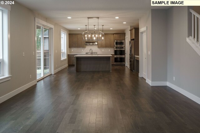 kitchen with hanging light fixtures, a kitchen island with sink, appliances with stainless steel finishes, and a wealth of natural light