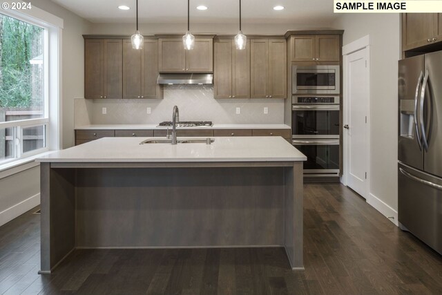 kitchen featuring appliances with stainless steel finishes, dark hardwood / wood-style floors, backsplash, and a kitchen island with sink