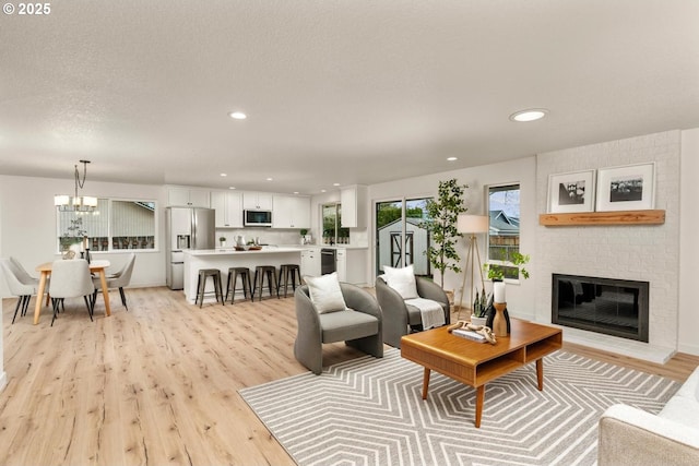 living area featuring light wood finished floors, recessed lighting, a fireplace, a notable chandelier, and a textured ceiling