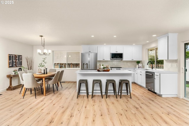 kitchen with a sink, stainless steel appliances, light countertops, a kitchen breakfast bar, and tasteful backsplash