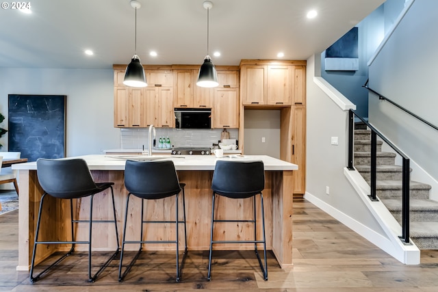 kitchen with light brown cabinetry, light hardwood / wood-style flooring, backsplash, and a center island with sink