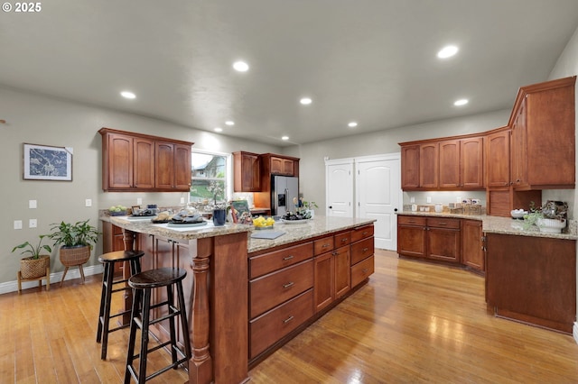 kitchen with light stone counters, light wood-type flooring, stainless steel fridge, and a kitchen island