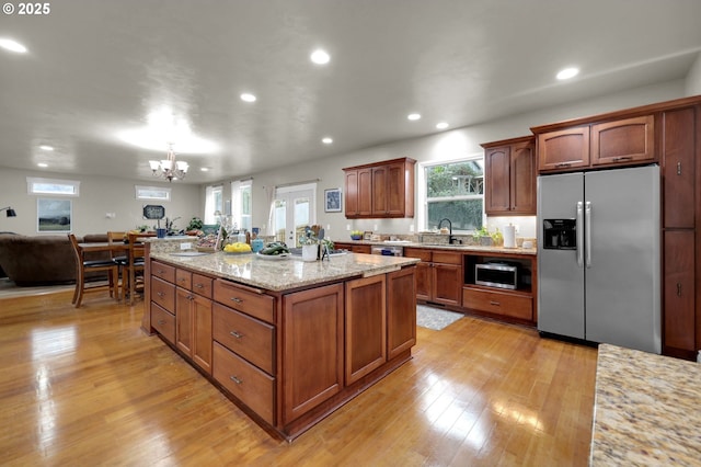 kitchen with sink, stainless steel appliances, light stone counters, light hardwood / wood-style floors, and a kitchen island