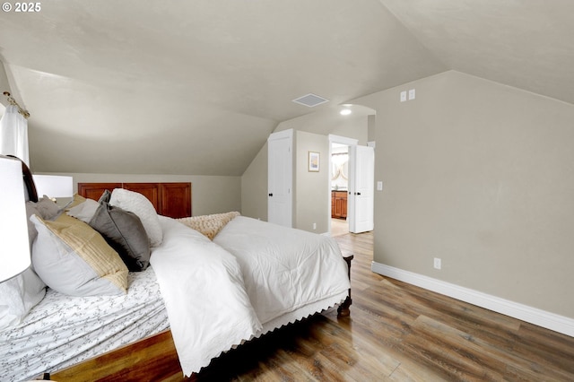 bedroom with hardwood / wood-style flooring, vaulted ceiling, and ensuite bathroom