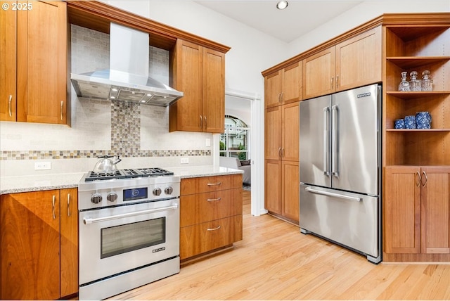 kitchen featuring backsplash, light stone counters, wall chimney exhaust hood, premium appliances, and light hardwood / wood-style floors