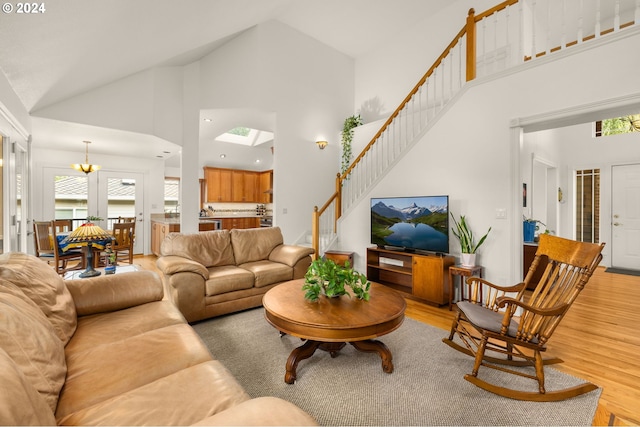 living room with light wood-type flooring, high vaulted ceiling, and a notable chandelier