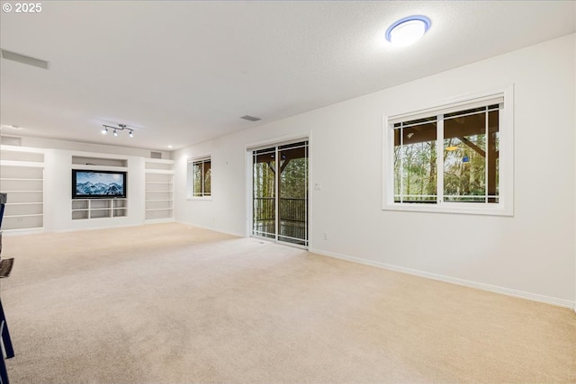 unfurnished living room featuring light carpet, built in features, a healthy amount of sunlight, and a textured ceiling