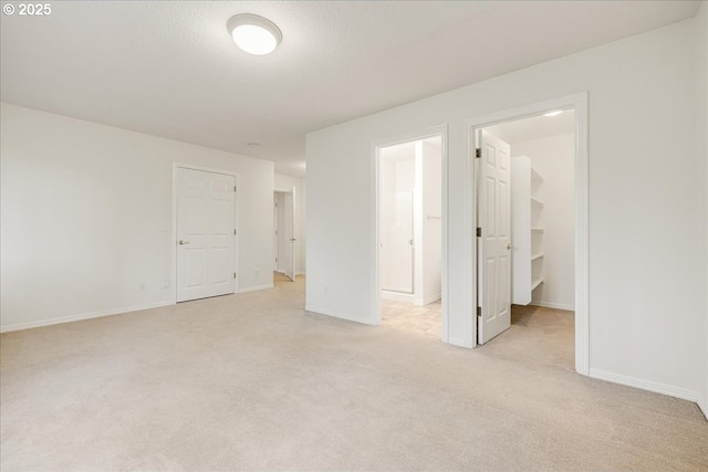 unfurnished bedroom with light carpet, ensuite bathroom, a spacious closet, a textured ceiling, and a closet