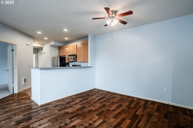 kitchen featuring ceiling fan, dark wood-type flooring, light stone counters, kitchen peninsula, and stainless steel fridge