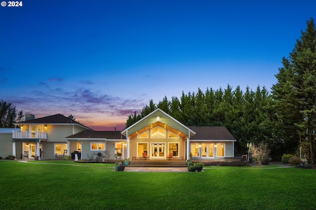 back house at dusk featuring a lawn