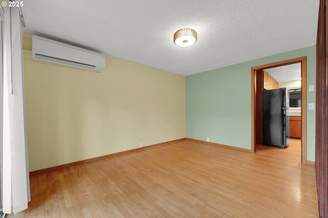 empty room with light wood-type flooring, a wall unit AC, and a textured ceiling