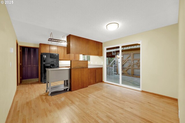 kitchen featuring black fridge, a textured ceiling, light hardwood / wood-style floors, and kitchen peninsula