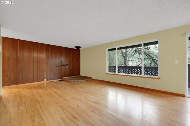 empty room featuring light hardwood / wood-style floors, wooden walls, and a textured ceiling