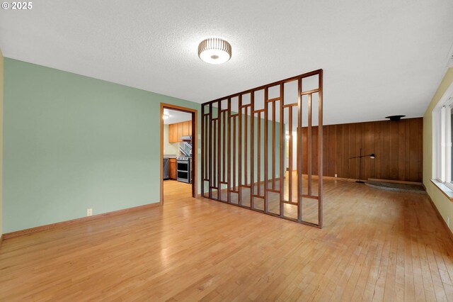 spare room with light hardwood / wood-style floors, wood walls, and a textured ceiling