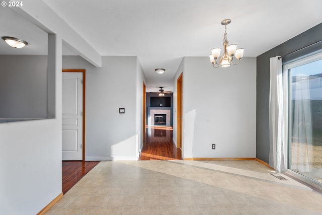 unfurnished room with a tiled fireplace, ceiling fan with notable chandelier, and light wood-type flooring