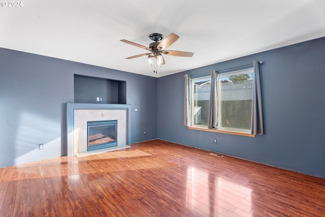 unfurnished living room featuring a tiled fireplace, ceiling fan, and hardwood / wood-style floors