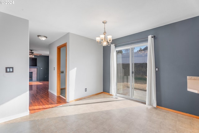 spare room featuring a fireplace, light wood-type flooring, and ceiling fan with notable chandelier