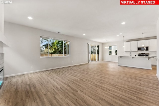 unfurnished living room featuring sink, a notable chandelier, a healthy amount of sunlight, and light hardwood / wood-style flooring