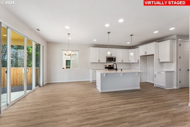 kitchen featuring an island with sink, white cabinetry, appliances with stainless steel finishes, light hardwood / wood-style floors, and tasteful backsplash