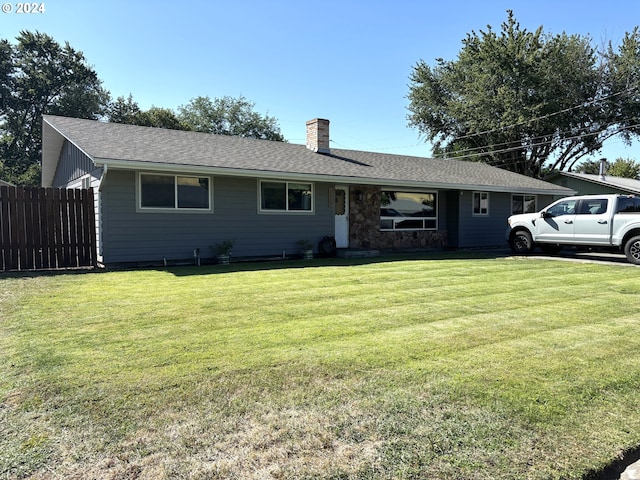 ranch-style house featuring a chimney, a shingled roof, a front yard, fence, and stone siding